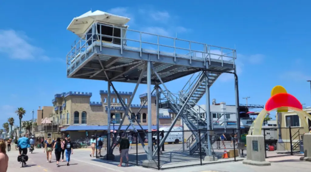 The structure features a traditional white lifeguard pod perched on top of a massive, multi-story web of steel scaffolding